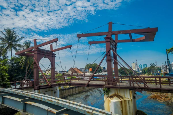 JAKARTA, INDONÉSIA: Charming canal de água passando por Jacarta visto com ponte de madeira na frente, edifícios de residência ao lado. belo céu azul — Fotografia de Stock