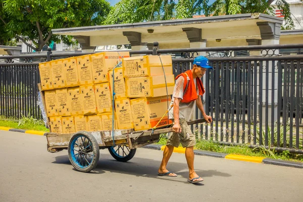 Jakarta, indonesien - 3. märz 2017: ortsansässiger arbeiter zieht Einkaufswagen voller pappkartons auf der straße — Stockfoto