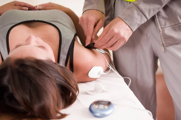 Närbild av en personlig tränare hand att sätta en electrostimulator elektroder i arm och axel av en kvinnlig deportist, liggande på ryggen — Stockfoto