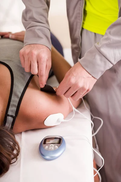 Gros plan d'une main d'entraîneur personnelle mettant un électrostimulateur électrodes dans l'épaule d'une déportiste féminine, à l'envers sur un lit — Photo