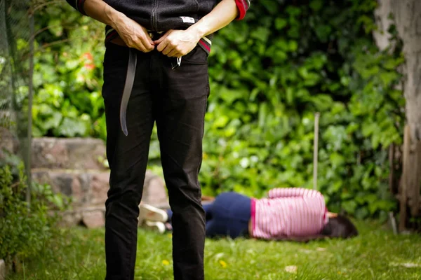 Primer plano de un hombre ajustándose los pantalones después de un abuso sexual, con una mujer tendida en el suelo detrás del violador. Concepto de violación y abuso sexual — Foto de Stock