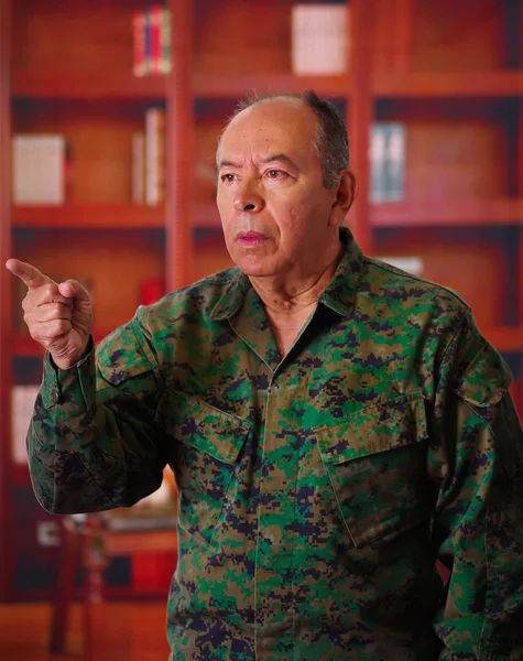 Acercamiento de un soldado veterano serio que llevaba un uniforme militar, señalando con su dedo en algún lugar en un fondo borroso — Foto de Stock
