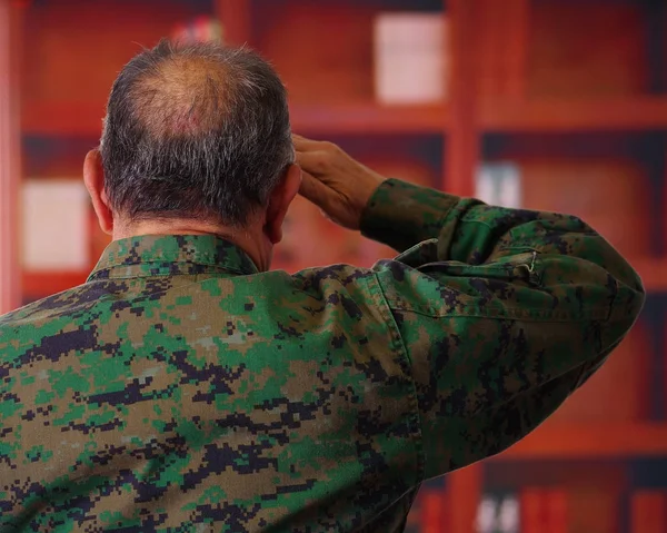 Acercamiento de un soldado veterano serio que llevaba un uniforme militar, haciendo una señal de saludo a la autoridad con su mano, dando una espalda en un fondo borroso —  Fotos de Stock