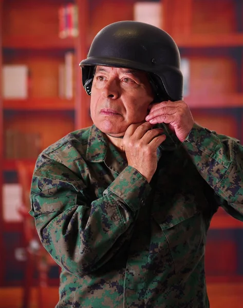 Close up of a serious veteran soldier wearing a helmet and a military uniform, with both hands adjusting the helmet, in a blurred background — Stock Photo, Image