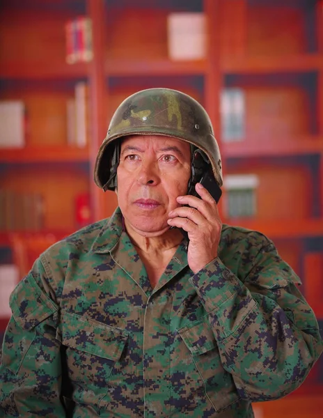 Крупним планом серйозного ветерана в шоломі і військовій формі, підвішуючи свій мобільний телефон на розмитому фоні — стокове фото