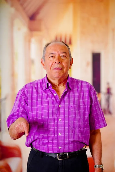 Close up de um velho feliz, apontando com a mão para baixo e vestindo uma camiseta quadrada roxa em um fundo borrado — Fotografia de Stock