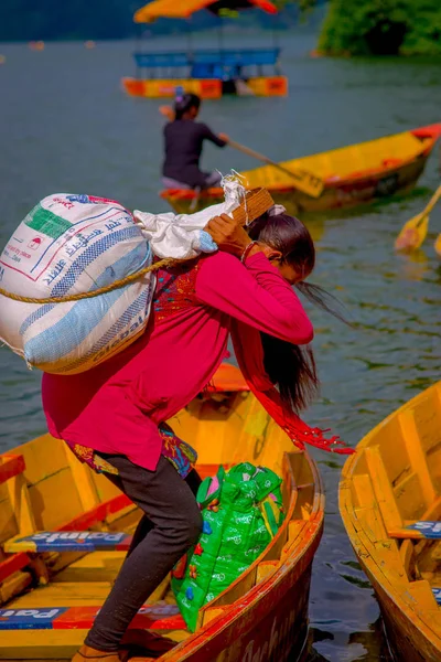 Pokhara, Nepal - 04 November 2017: Close up up van sterke vrouw die in haar rug een zware zak lopen over een gele boot op Begnas meer in Pokhara, Nepal — Stockfoto