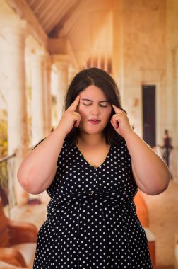 Her ikisi de eller, xxl kadın gri studio arka planda, tam uzunlukta portre onun baş bith dokunaklı siyah dres bir baş ağrısı olan genç boyutu güzel model