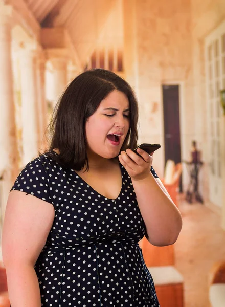 Jovem modelo bonito plus size em preto dres, usando seu celular, mulher xxl no fundo do estúdio borrado — Fotografia de Stock