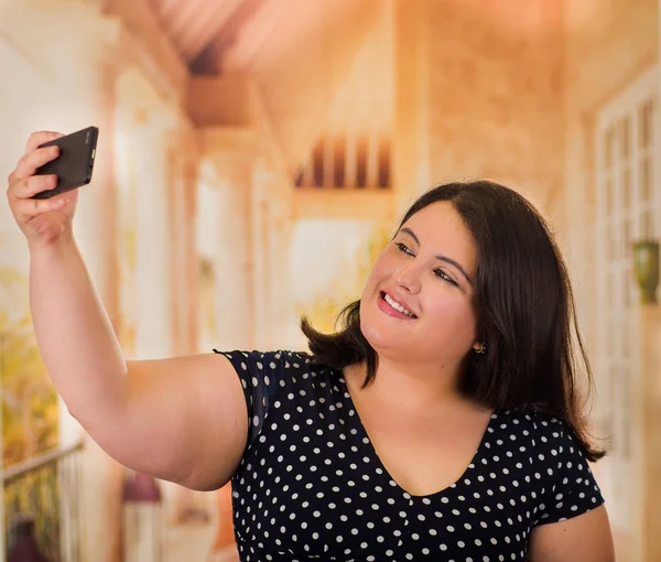 Young beautiful plus size model in black dres, taking herslef a selfie with her cellphone, xxl woman on blurred studio background — Stock Photo, Image