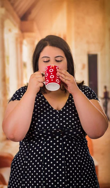 一个漂亮的胖女人在一个美丽的礼服, dra 杯咖啡在一个模糊的背景 — 图库照片