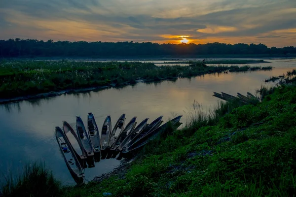 Hermosa puesta de sol en el Parque Nacional de Chitwan, con algunos barcos en una fila en el río, yhis hermoso lugar está cubierto principalmente por la selva — Foto de Stock