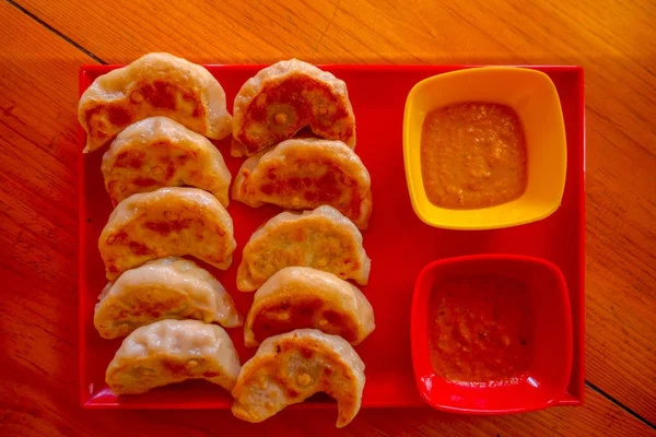 Oben Blick auf gedämpftes Essen momo, mit einer gelben und roten Schüssel mit Sauce. eine beliebte nepalesische Speise, die auch in Chiana, Bhutan, Tibet und Indien verbreitet ist, vor einem hölzernen Tischhintergrund — Stockfoto