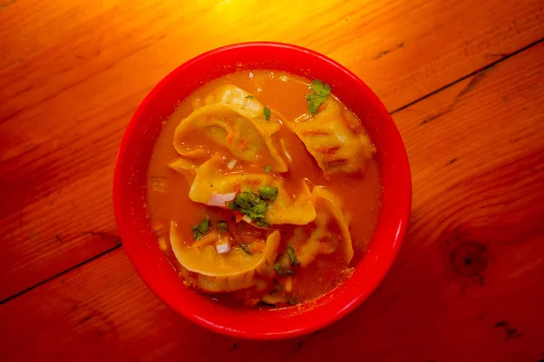 Vista dall'alto della zuppa al vapore di Momo servita in una ciotola rossa. Un cibo popolare nepalese che è comune anche in Chiana, Bhutan, Tibet e India, in uno sfondo tavolo di legno — Foto Stock