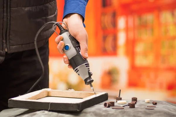 Close-up van een man van de hardworker boren van een houten frame met zijn boor, met toebehoren boren op een grijze tabel in een onscherpe achtergrond — Stockfoto