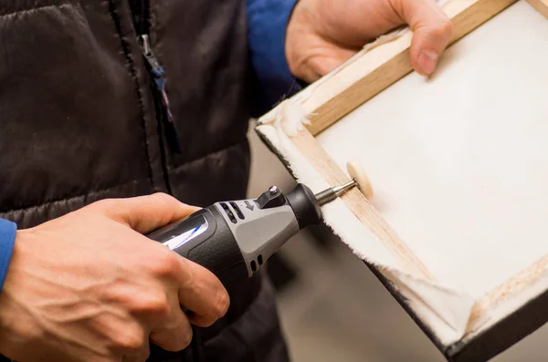 Close-up van een hardworker man een frame met de ene hand te houden en met behulp van een polijstmachine in een houten frame met zijn andere hand — Stockfoto