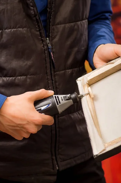 Close-up van een hardworker man een frame met de ene hand te houden en met behulp van een polijstmachine in een houten frame met zijn andere hand — Stockfoto
