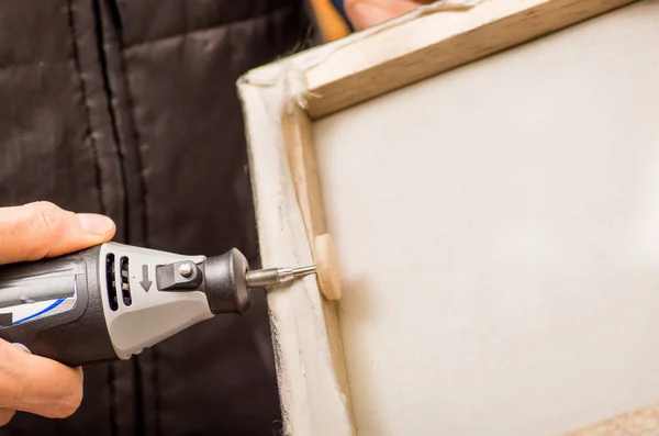 Close-up van een hardworker man een frame met de ene hand te houden en met behulp van een polijstmachine in een houten frame met zijn andere hand — Stockfoto