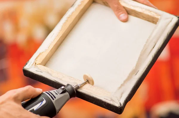 Close-up van een hardworker man een frame met de ene hand te houden en met behulp van een polijstmachine in een houten frame met zijn andere hand in een onscherpe achtergrond — Stockfoto