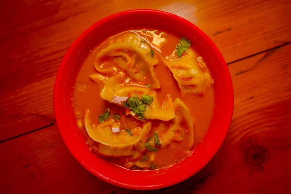 Vista superior de la sopa al vapor de Momo servido en un tazón rojo. Una comida popular nepalí que también es común en Chiana, Bután, Tíbet e India, en un fondo de mesa de madera — Foto de Stock