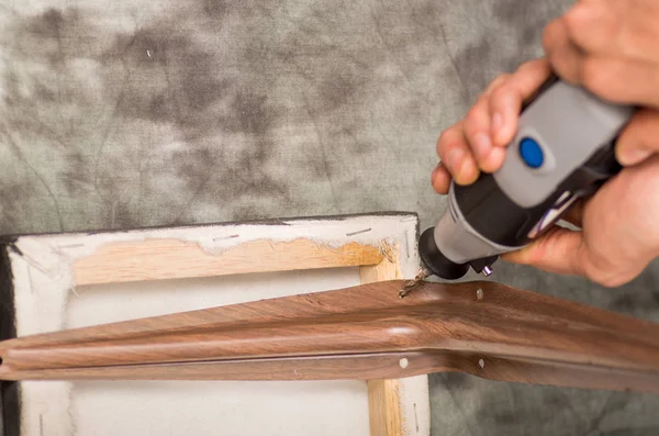 Close-up van een man van de hardworker boren een een metalen stuk in een houten frame met zijn boor, in een grijze achtergrond, bovenaanzicht — Stockfoto