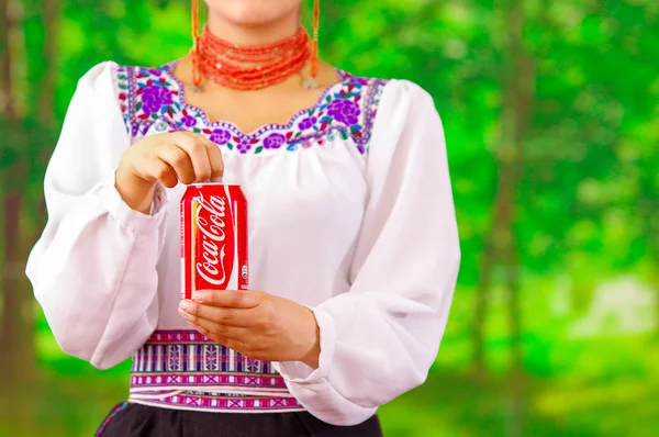 Quito, Ecuador - 06 maj 2017: Ung kvinna bär en inhemska kläder och pekar i från henne en coke medan hon är öppna det, i en skog bakgrund — Stockfoto