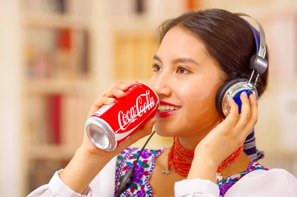 Quito, Équateur - 06 mai 2017 : jolie jeune femme autochtone qui boit de la coke alors qu'elle utilise un casque — Photo