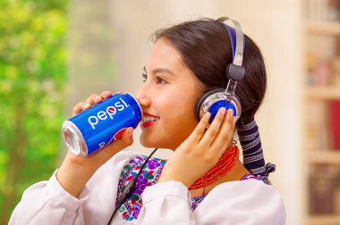 Quito, Ekvator - 06 Mayıs 2017: Kulaklık kullanırken bir pepsi içme genç yerli kadın güzel