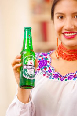 Quito, Ekvator - 06 Mayıs 2017: güzel bir gülümseyen kadının elinde bir şişe Heineken bira bir orman arka planda elinde iken yerli bir giyim eşyası kapat