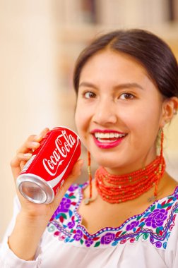 Quito, Ecuador - May 06, 2017: pretty young indigenous woman drinking a coke while she is smiling clipart