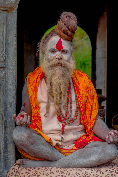 KATHMANDU, NEPAL - MARCH 22, 2017: Close up of Yogi Shaiva sadhu sitting in Pashupatinath Temple of Kathmandu with his legs crossed, in Nepal