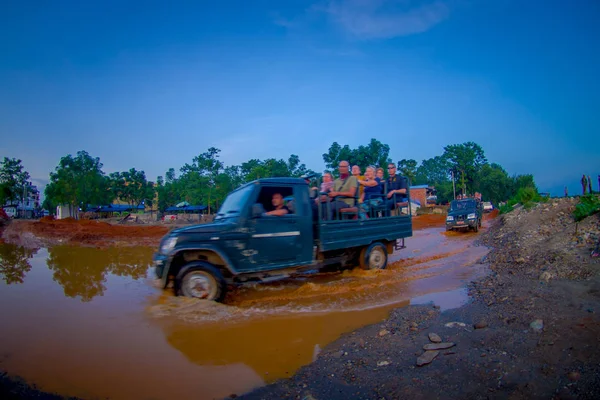 CHITWAN, NEPAL - NOVEMBER 03, 2017: Unidentified people traveling in the back part of a car, crossing a street with dirty water, happy tourists for jungle safari at Chitwan National Park, Nepal, fish — Stock Photo, Image