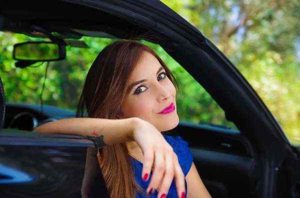 Retrato de mulher bonita vestindo um vestido azul e posando dentro de um carro preto de luxo em uma viagem, o carro de pé nas laterais, em um fundo natureza turva — Fotografia de Stock