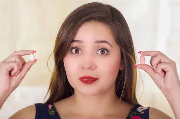 Portrait of a confused woman holding in both hands a soft gelatin vaginal tablet or suppository, treatment of diseases of the reproductive organs of women and prevention of womens health, in a — Stock Image Portrait of a confused woman holding in both hands a soft gelatin vaginal tablet or suppository, treatment of diseases of the reproductive organs of women and prevention of womens health, in a Stock Picture