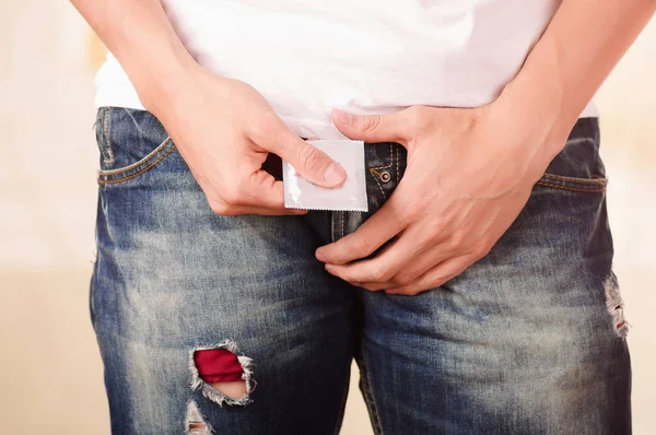 Close up of man holding a condom with one hand and holdings his private parts in front of his jeans between his legs, a sign of a safety sex — Stock Photo, Image