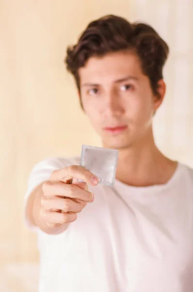Acercamiento de un hombre borroso señalando delante de él un condón, un signo de un sexo seguro en un fondo borroso —  Fotos de Stock