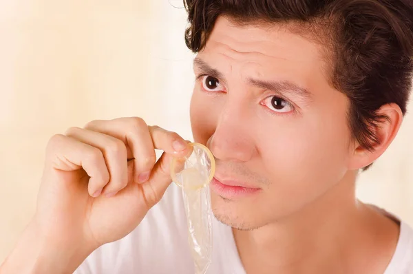 Retrato de homem bonito preocupado segurando um preservativo aberto com uma mão e cheirando na frente do rosto, um sinal de doença sexual, em um fundo embaçado — Fotografia de Stock