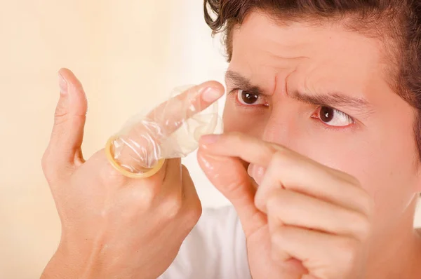 Porträtt av orolig man hålla en öppen bruten kondom med ena handen framför ansiktet och att vidröra den trasiga bit med sin andra hand, ett tecken på sex sjukdom, i en suddig bakgrund — Stockfoto