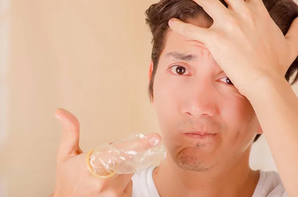 Porträtt av orolig man hålla en öppen bruten kondom med ena handen framför ansiktet och att röra sitt huvud med sin andra hand, ett tecken på sex sjukdom, i en suddig bakgrund — Stockfoto