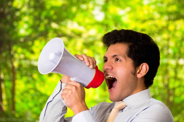 Retrato de um homem bonito gritando com um megafone em um fundo verde borrado — Fotografia de Stock