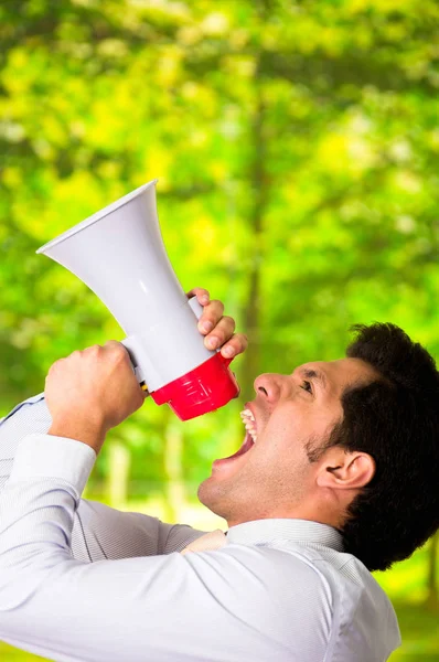 Portret van een knappe man met een megafoon in een wazig groene achtergrond schreeuwen — Stockfoto