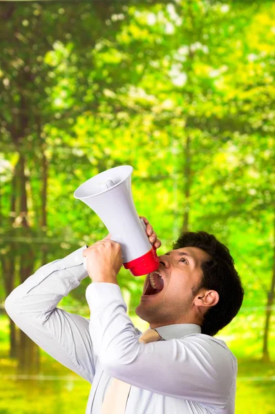 Retrato de um homem bonito gritando com um megafone em um fundo verde borrado — Fotografia de Stock