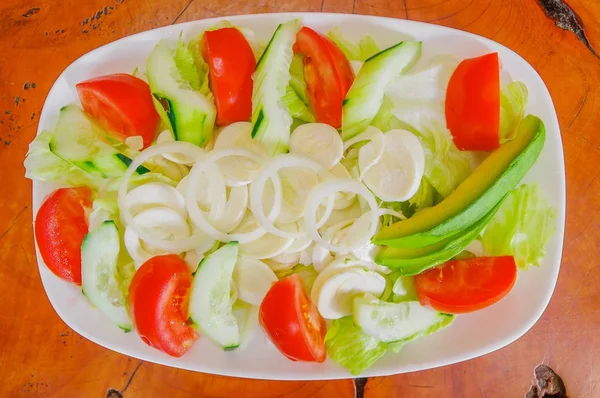 Above view of fresh salad with vegetables, tomato, onion, palmito, cucumbers, served on a white plate on wooden table — Stock Photo, Image