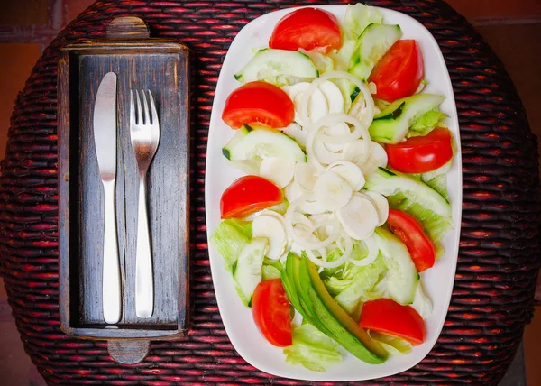 Above view of fresh salad with vegetables, tomato, onion, palmito, cucumbers, served on a white plate with a fork and knife in the table, on wooden table — Stock Photo, Image