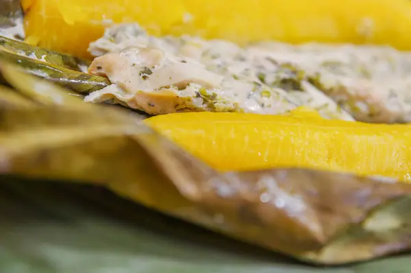 Gros plan de délicieux plats typiques de l'Amazonie, poisson cuit dans une feuille de yucca et plantain, servi dans une assiette en bois sur une table en bois — Photo