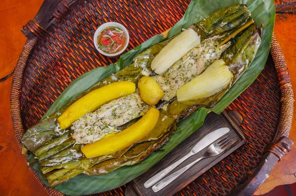 Ovanför vyn av läckra typiska Amazonas mat, fisk tillagas i ett blad med yucca och groblad, skål med sallad, serveras i en träplatta över ett träbord — Stockfoto