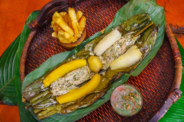 Ovanför vyn av läckra typiska Amazonas mat, fisk kokt i ett blad med yucca och groblad, skål med sallad och friterad yucca, serveras i en träplatta över ett träbord — Stockfoto