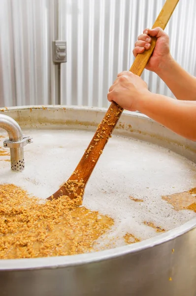 Primo piano di pala in legno con chicchi di grano all'interno di un moderno bollitore, vasi, in un impianto di birra a Quito — Foto Stock