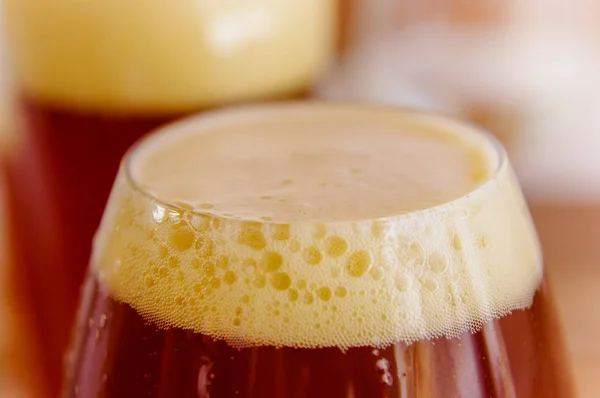 Close up de vidro de cerveja escura com espuma em um fundo embaçado — Fotografia de Stock