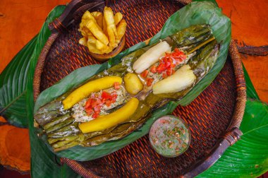 Görünümü lezzetli tipik Amazon yiyecek bir yaprak avize ve muz, salata ve kızarmış yucca, kase pişmiş balık ahşap bir tabak içinde ahşap bir masaya servis